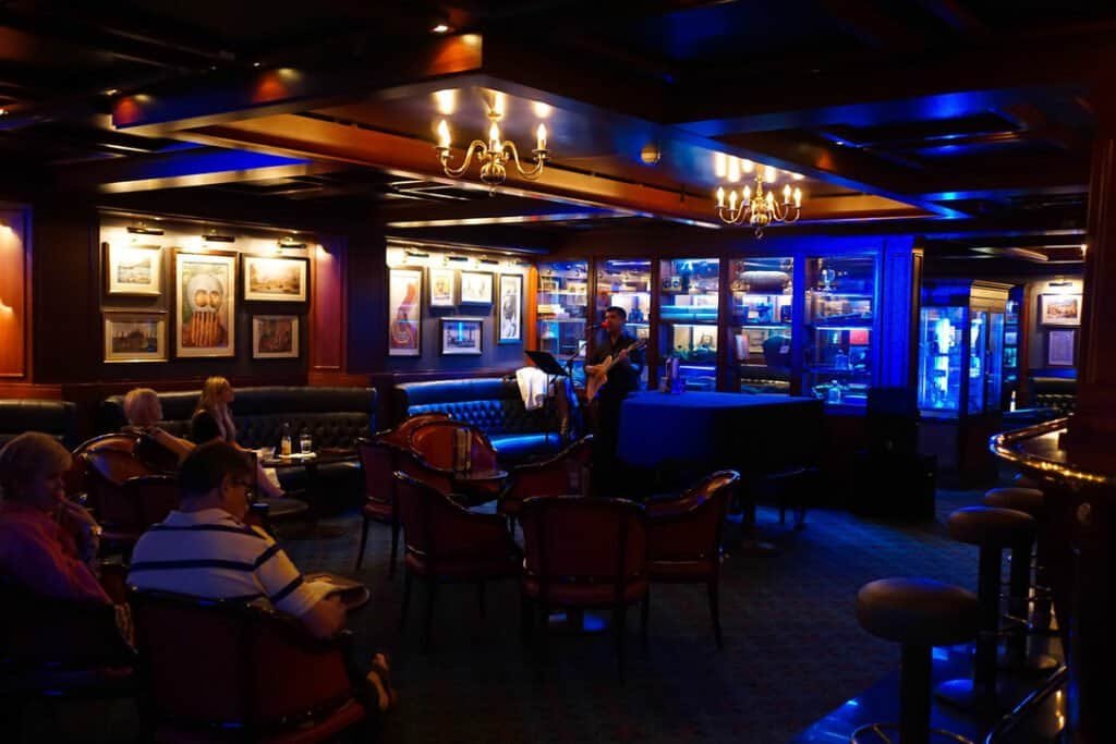 Cruise lounge scene with guests relaxing and live entertainment on Norwegian Sky.