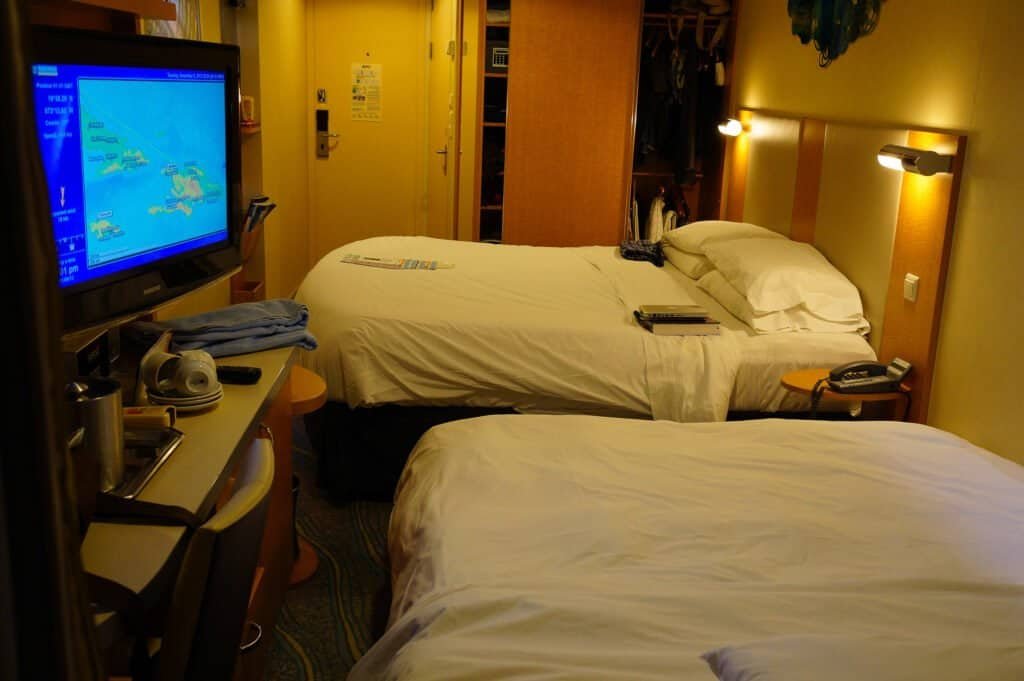 Cruise ship cabin featuring two beds, TV, and cozy decor for a relaxing voyage.