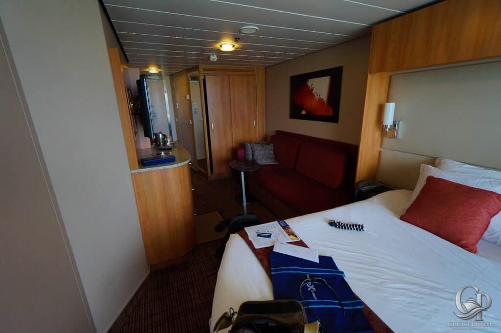Celebrity Silhouette Cruise ship cabin interior with bed, sofa, and wooden accents.