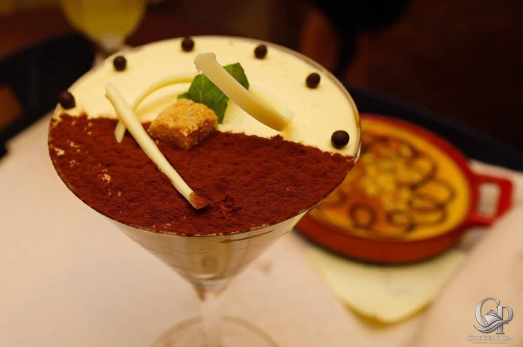 Delicious tiramisu served in a glass with cocoa powder, white chocolate, and mint garnish, aboard Celebrity Silhouette.