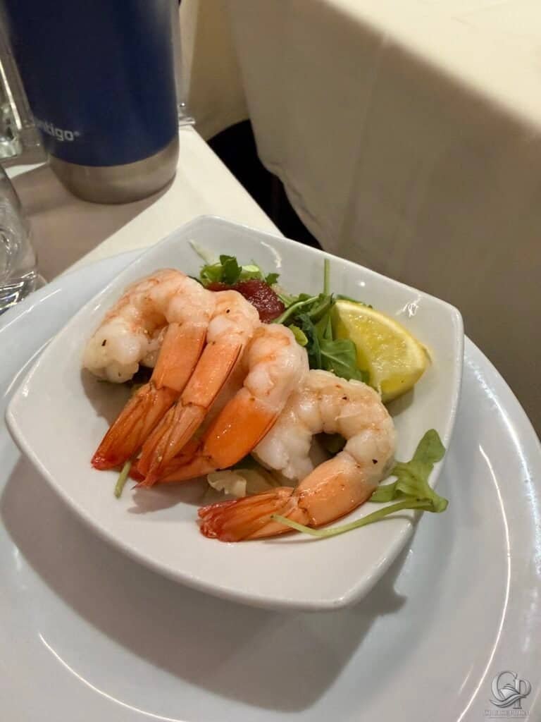 Fresh shrimp cocktail served with lemon wedge and greens on a white dish aboard MSC Seaside.