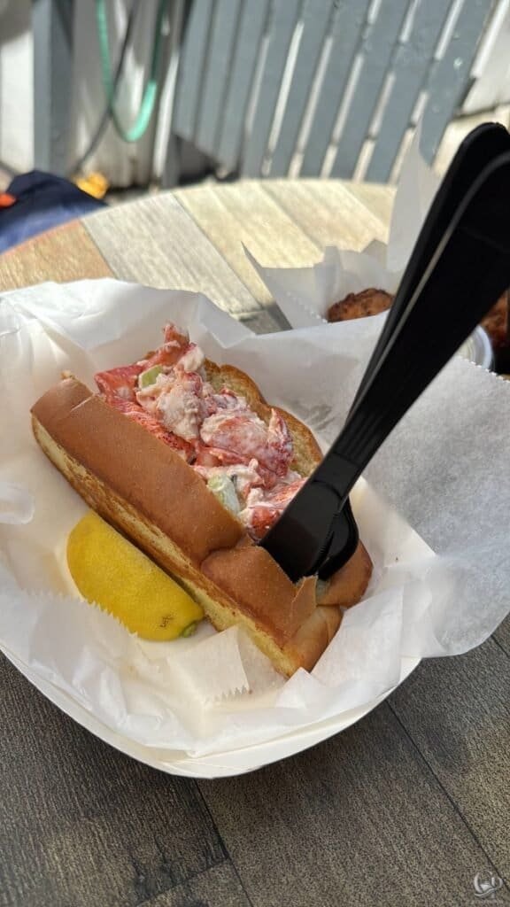 DJ's Clam Shack, Delicious lobster roll served with lemon wedge on a wooden table.