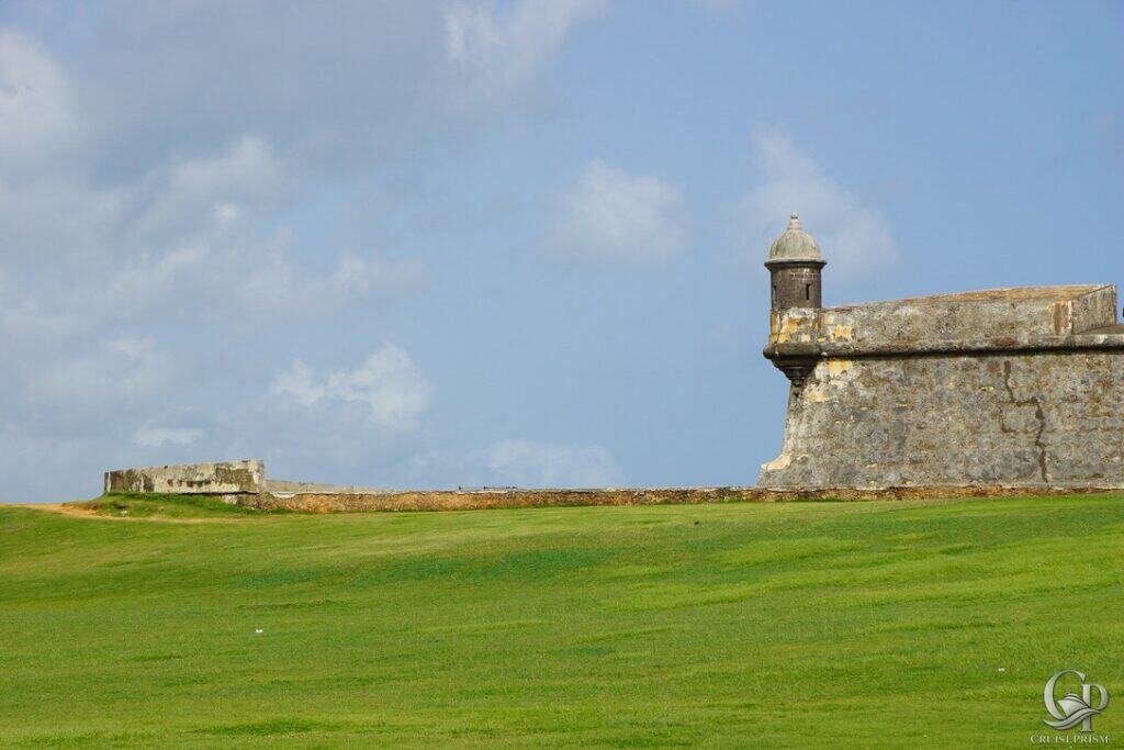 Fortress on green landscape with historic stone structure and watchtower under blue sky.