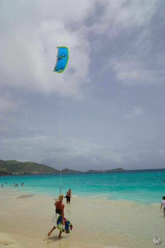 Kite surfer flying a colorful kite over turquoise waters on a sunny beach.